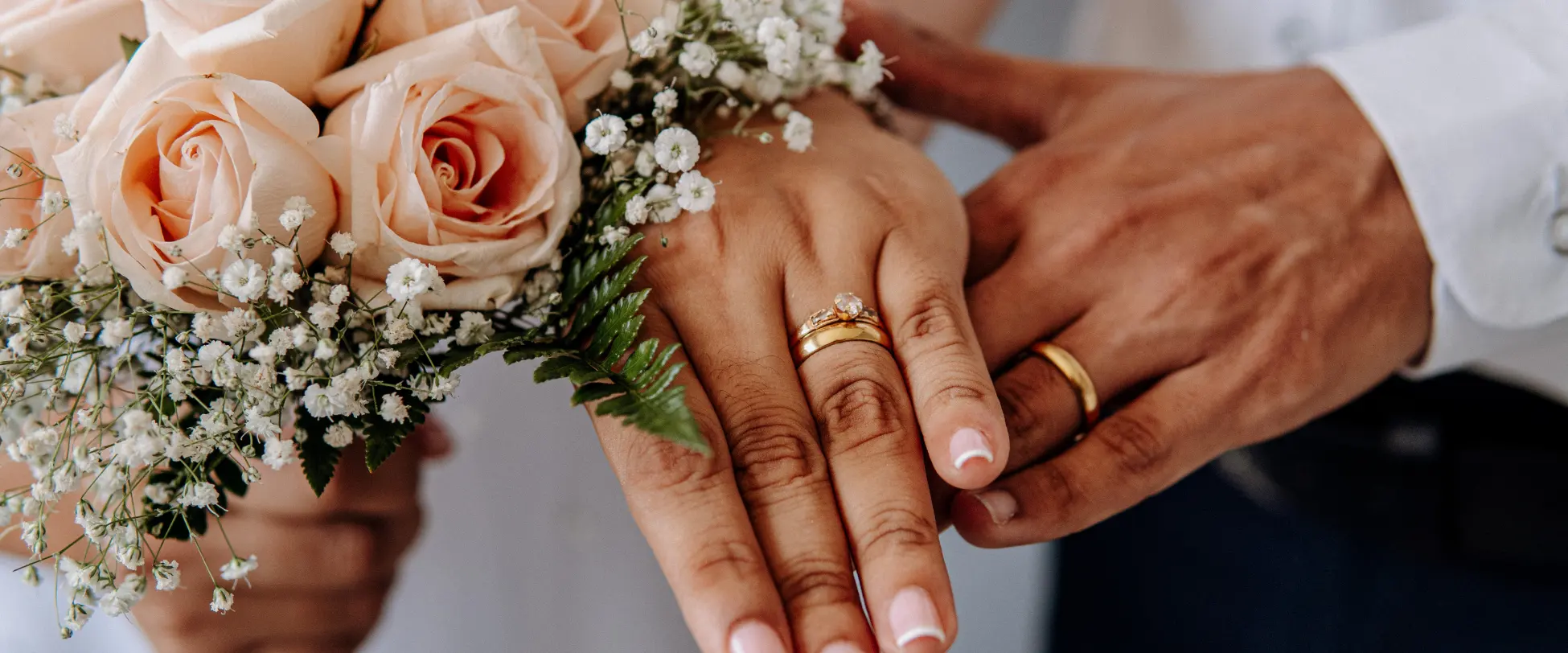 A newly married couple's hands, complete with rings and a bouquet of pink flowers..