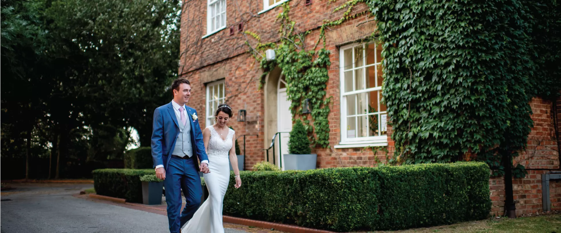 A bride and groom walk hand in hand outside a gorgeous Georgian building, the Holiday Inn Milton Keynes East.